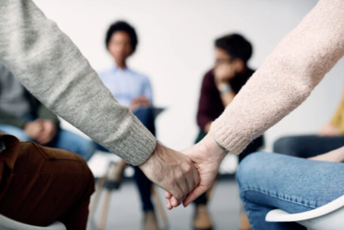 Close-up of couple holding hands while attending psychotherapy with group of people.